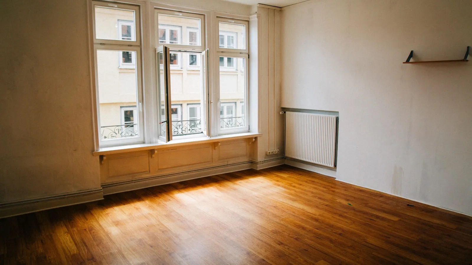 Lege kamer met een houten vloer en een groot raam met daglicht.