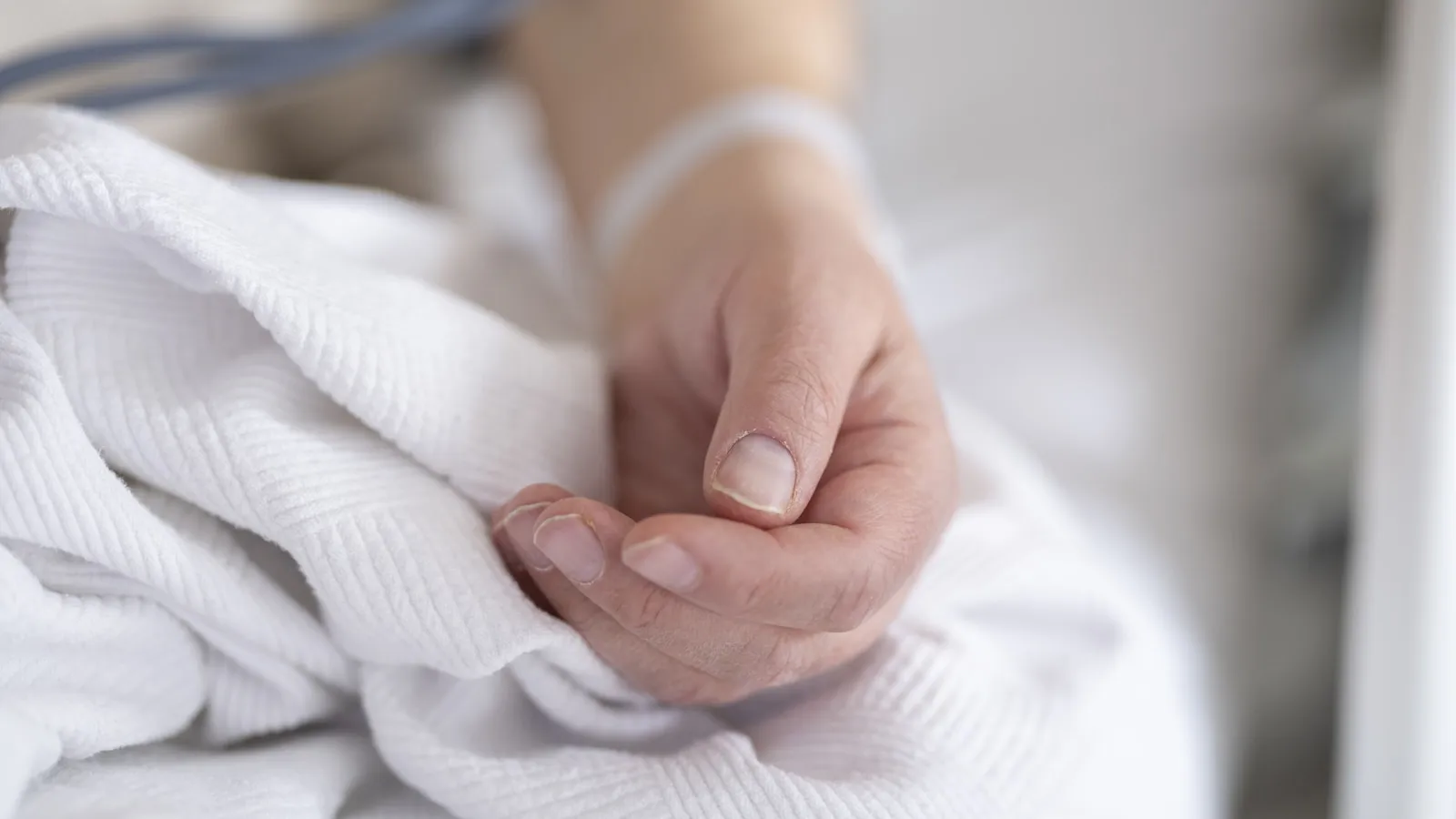 Een hand die rust op wit beddengoed in een ziekenhuisbed.