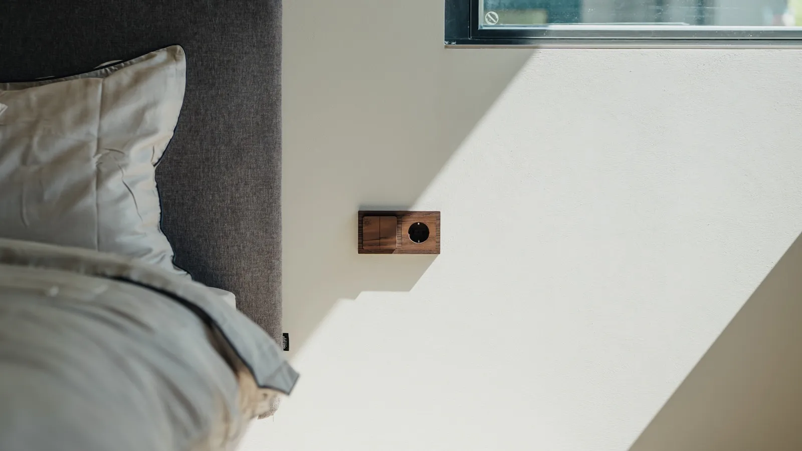 Ochtendlicht dat over een witte muur naast een opgemaakt bed valt.